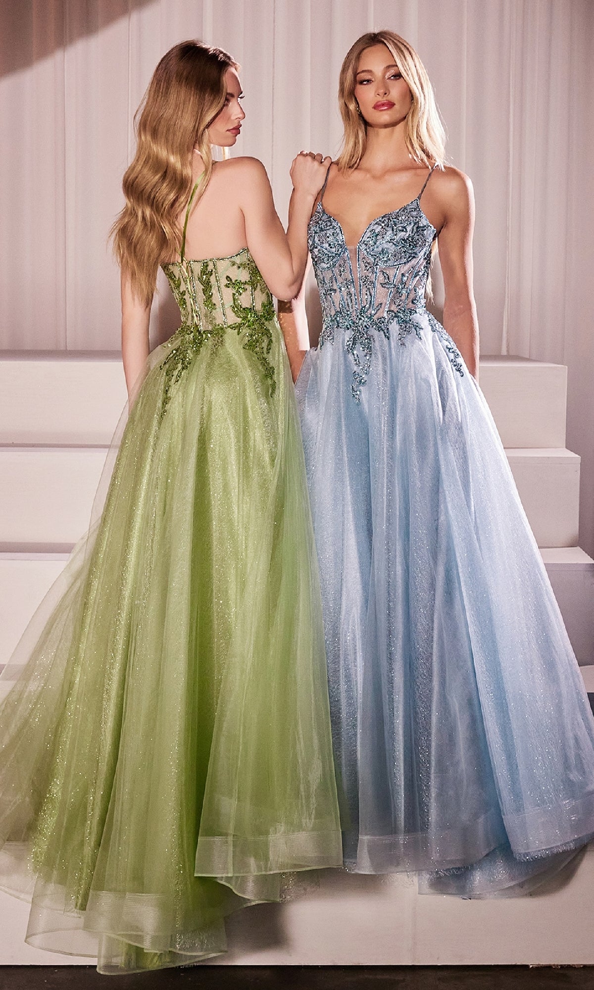 Two women in formal gowns stand side by side; both wear the Sheer-Corset Long Prom Dress: Ladivine CC0881, one in green with floral details, the other in blue with beaded embroidery. Both feature elegant tulle skirts.